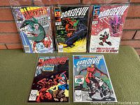 Five Daredevil comics arranged on green surface against brick background, showing cover art and set completeness.