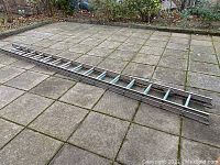 Full view of the 20-foot aluminum extension ladder laid flat on a paved outdoor surface, showing its length and overall condition.