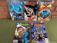 Five Batman Detective Comics issues laid out on surface, arranged in two rows showing various cover art.