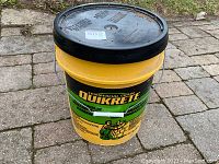 Full yellow and black bucket labeled Quikrete Commercial Grade Hydraulic Water-Stop Cement.
