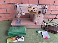 Singer 328 K electric sewing machine with green accessory case, buttonholer instructions, foot pedal, and packaged buttons on surface next to machine.