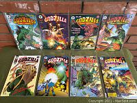 Photo showing all 8 Godzilla King of Monsters comic books arranged in two rows against a brick background, each sealed in plastic.