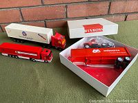 Four diecast promotional transport trucks displayed side by side, one in original Winross box with cover removed.