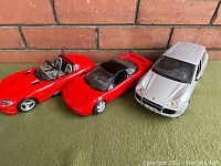 Photo showing three diecast vehicles: red convertible, red coupe, silver SUV, placed on green surface