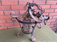 View of the light fixture showing the wrought iron curved top and chain, along with the patterned glass shade inside.