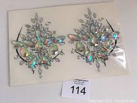 Photo of two symmetrical sets of clear iridescent rhinestone body gem stickers on adhesive backing inside clear plastic packaging.