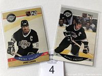 Front of two Wayne Gretzky NHL Pro Set hockey cards in Los Angeles Kings black jersey with 'C' captain patch. One card has a red and blue banner at bottom edge with his name and position 'Point Leader'. The other shows Gretzky skating with stick on ice.
