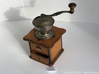 Wooden coffee mill with metal grinder and handle on top, small drawer below, showing full front and top angle.