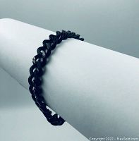 Black chain link bracelet displayed on white cylindrical holder to show style and shape.