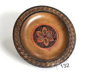 Overall view of one decorative round wooden plate showing the hand carved floral design, brass inlaid wire, and carved border edge.