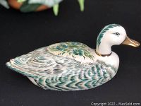 Full side view of white porcelain duck figurine with green hand painted feather pattern and floral decoration on back.