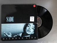 Front cover of Sade's Diamond Life vinyl record album sleeve with record partially visible.