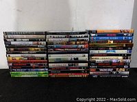 Photo showing 30 assorted DVDs stacked upright with titles visible including Cloverfield, The Departed, Gladiator, and others.