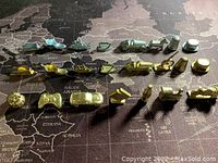 Metal Monopoly game pieces arranged in rows by set on world map background, displaying variety of token shapes and finishes