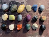 Eighteen assorted collectible stones displayed on a world map background, showing variety in shapes, colors and textures.