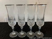 Four crystal champagne flutes in a row showing faceted diamond pattern around the bottom half and vertical cuts above, standing on a flat surface.