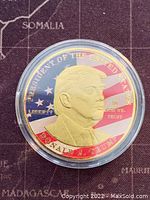 Obverse side of the gold tone medallion showing Donald J. Trump's profile with American flag background and inscriptions