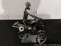 Side view of metal figurine showing person sitting on detailed motorcycle with exhaust and helmet.