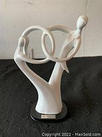 Front and side views of white statue of a couple dancing with intertwined arms on black base with a silver plaque.