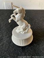 Side angled view of white ceramic unicorn figure on round ridged base on black surface.
