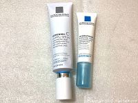 Photo of two white tubes labeled La Roche-Posay Redermic C and Hydraphase Intense Eye against a beige background.