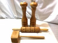 Four vintage wooden kitchen items on display against white cloth backdrop showing two tall salt and pepper mill shakers, a carved Springerle rolling pin, and a wooden meat tenderizer mallet.