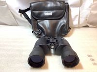 Front view of binoculars lying on surface with carrying case behind
