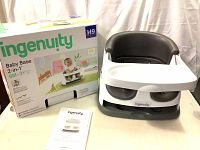 White and gray Ingenuity Baby Base 2-in-1 Baby Feeding Chair with tray and manual next to original box showing branding and age suitability 6 months to 3 years.