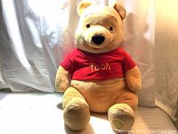 Front view of large Winnie the Pooh plush toy wearing red 'Pooh' shirt.