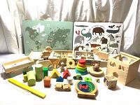 Photo showing all wooden toys including puzzles, shape sorter, stacking rings, animal figures, and wooden vehicles arranged together.