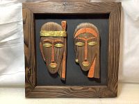 Front view of the two carved wood tribal masks mounted in the rustic wooden frame.