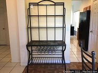 Full front view of the metal baker's rack showing tile top, multiple shelves, and the wine rack.