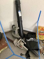 Earthwise electric blower with black attachments and collection bag, Craftsman bushwacker on floor next to it.