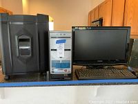 Emachines computer tower, Sylvania monitor, keyboard, and mouse displayed on counter with PenGear shredder to the side.