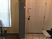 Gray plastic wood grain shutter standing upright against wall with a door and window nearby.