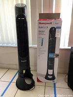 Full view of the Honeywell QuietSet 5 tower fan standing next to its original retail box on tile floor. Fan is black and about 40 inches tall.