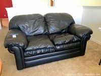Front view of black leather look loveseat with two seat cushions and padded armrests.