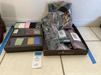 Photo of assorted new men's neckties and boxed gift sets arranged on the floor, showing various patterns and unopened packaging.