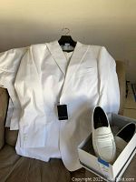 Full view of white Paul Fredrick men's suit jacket laid over couch, with an adjacent shoebox containing white slip-on loafers.