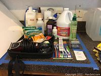 Photo showing Oster electric clippers with cord, various hair care and cleaning bottles including bleach and Pantene shampoo/conditioner, Glade spray, and bathroom scale.