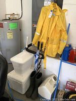 Yellow Master Gear rain jacket and pants hanging near water heater with black rain boots, coolers, and umbrellas arranged below