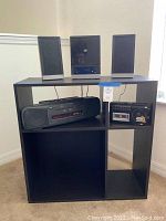 Full view of shelf unit with stereo system components on and inside it. Two stereo speakers, mini CD/radio player on top shelf, RCA boombox and portable cassette player inside compartments.