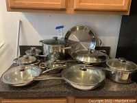 Overview of the entire assortment of pots and pans with lids arranged on countertop