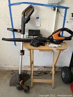 Photo of the Worx trimmer/edger lying horizontally on a small wooden table with charging station, battery, and power cord visible
