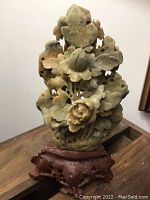 Front view of the carved stone sculpture showing detailed flowers and leaves on a carved wooden base.