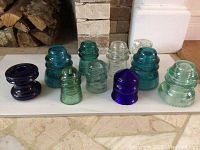 Front view of nine used glass electrical insulators in multiple colors and shapes arranged on a white surface.
