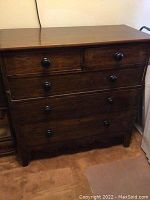 Front view of dark stained hardwood dresser with four drawers and round wooden knobs, showing scratches and wear.