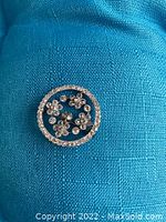 Front view of round platinum brooch showing floral openwork and diamond setting.