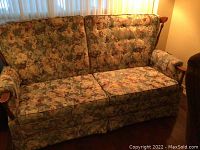 Frontal view of floral upholstered sofa bed showing three seat cushions, button tufted back cushions, and wooden armrests.