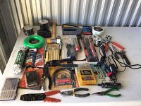 Overview of mixed hand tools, drill bits, pliers, stapler, measuring tape, hammer, and assorted accessories arranged on a white surface.